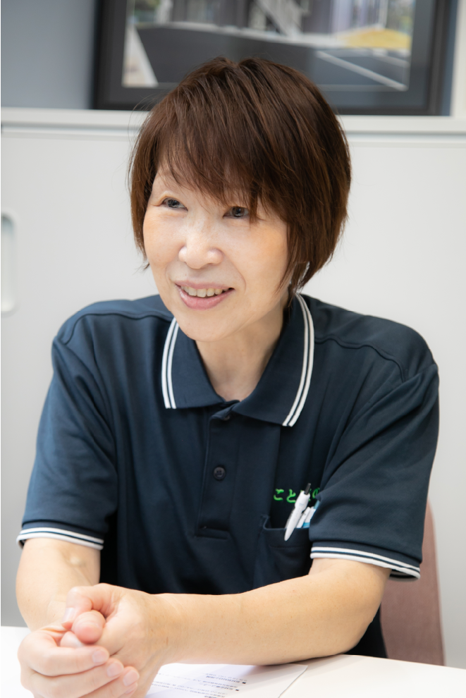 ことばの道スタッフ・代表理事・安居道子 ショートカットの清潔感のある優しげな女性が白い背景を前に話している